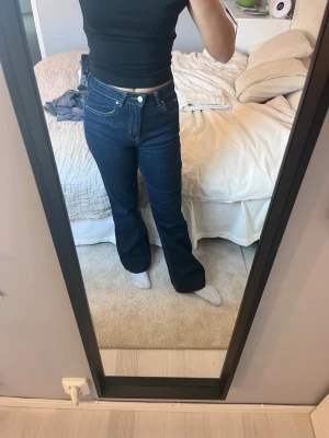 Mörkblå bootcut jeans med medelhög midja - Säljer ett par mörkblå bootcut jeans med medelhög midja. Jeansen har en snygg passform som framhäver benen och är tillverkade i ett stretchigt denim-material. Perfekta för dig som gillar en tidlös och trendig look.