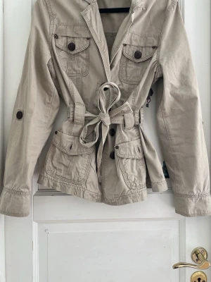 Snygg beige y2k trenchcoat - Super snygg beige kort trenchcoat. Mycket fin som en vårjacka så den är ganska tunn!