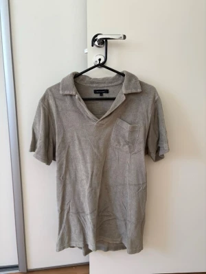 Beige frottéskjorta från Paul & Shark - Säljer en beige skjorta från Paul & Shark i frottématerial med korta ärmar och klassisk krage. Skjortan har en bröstficka och en avslappnad passform som är perfekt för en chill look. Perfekt för dig som gillar stilrena plagg med lite extra känsla.