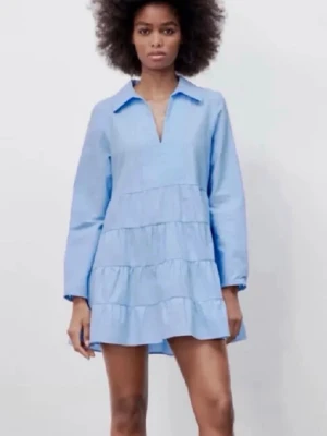 Ljusblå volangklänning från Zara - Säljer en ljusblå kortklänning från Zara med volanger och lång ärm. Klänningen har en avslappnad passform, krage och v-ringad hals. Perfekt för sommarens alla tillfällen och tillverkad i mjuk bomull.