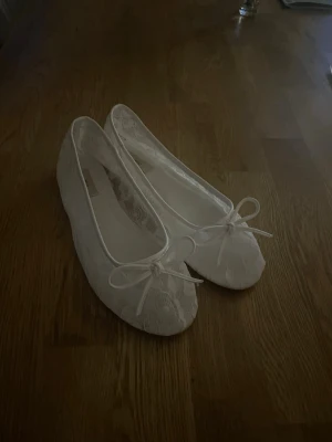 Vita spetsballerinaskor med rosett - Snygga vita ballerinaskor täckta med spets och en rosset framtill. Använda en gång, säljes pga att de är förstora. Ny pris 349kr