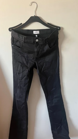 Svarta bootcut jeans från ONLY - Snygga svarta bootcut jeans från ONLY med klassisk femficksdesign och knappgylf. Jeansen har en smal passform upptill och lätt utsvängda ben. Perfekta till en trendig vardagslook och passar till det mesta. Materialet känns mjukt och stretchigt.