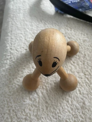 Träfigur   Massage - Detta är ett massageverktyg i trä format som en mus. Det har fyra ben med runda "fötter" som kan användas för att massera olika delar av kroppen. Musen har ett målat ansikte med ögon, nos och morrhår, samt en svans av läder.