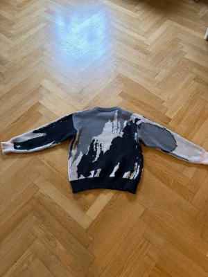 Stickad tröja med abstrakt mönster - Cool stickad tröja med abstrakt mönster i svart, grått, beige och vitt. Tröjan har rund halsringning och ribbstickade muddar vid ärmslut och nederkant. Perfekt för dig som gillar unika plagg med streetkänsla.