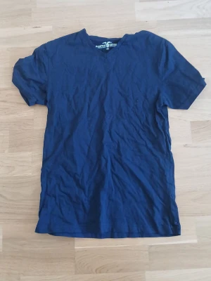 Marinblå T-shirt - En enkel marinblå T-shirt med V-ringning och korta ärmar. Tillverkad i mjuk bomull som känns skön mot huden. Perfekt basplagg för alla tillfällen och lätt att matcha med andra plagg. Aldrig använd och ser helt ny ut.