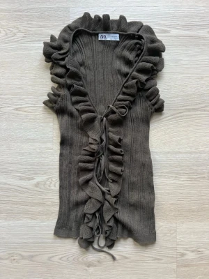 Brun/grön  ribbad volangtopp från Zara - Supersnygg brun ribbad topp från Zara med volangkant längs v-ringningen och framtill. Toppen har knytband framtill och är ärmlös, perfekt för att lyfta din outfit med en trendig touch.