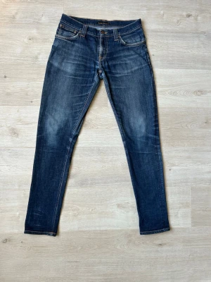 Blåa Nudie Tight Long John Jeans Storlek W30 L32 - Fina Nudie Jeans i blå färg. Jeansen är i mycket bra skick och sparsamt använda.  Äkta som allt annat jag säljer! ✅  Storlek: W30 L32 Skick: Mycket Bra Skick - lagad vid ett ställe,  (SE SISTA BILD) Färg: Blå Märke: Nudie Modell: Jeans    Hör gärna av dig vid frågor så svarar jag så fort jag kan! 😁  (SKU - 101)
