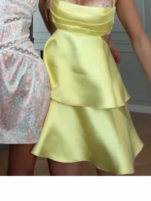 Gul klänning med volang - Superfin gul kortklänning med omlottdesign och volangdetaljer. Klänningen har smala axelband som korsas i ryggen och är tillverkad i ett glansigt material som ger en lyxig känsla. Perfekt för dig som vill sticka ut med en färgglad look. Strlk L men passar även M