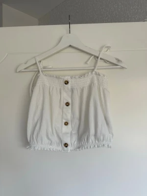 Topp - Kort linne/topp med knytning på axlarna och resår både upp- och nertill. Knapparna är endast dekoration