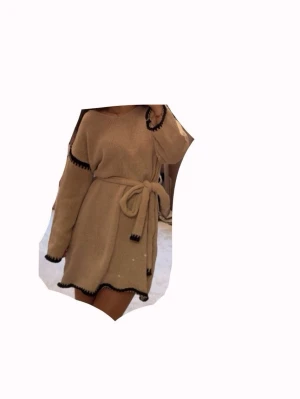 Beige stickad klänning med svarta detaljer - Mysig beige stickad klänning med svarta kanter och knytband i midjan. Långärmad och med avslappnad passform. Materialet är mjukt och ger en skön känsla mot huden. Snygg kontrast med de svarta detaljerna på ärmar och nederkant. Endast använd 1 gång!🩷