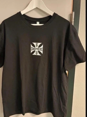 Svart West Coast Choppers t-shirt - Svart t-shirt från West Coast Choppers med stort vitt tryck på ryggen och mindre tryck på bröstet. Klassisk rund hals och rak passform. Perfekt för dig som gillar streetwear och bikerstil. Large men passar medium 