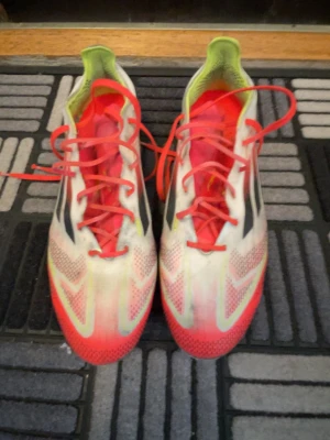 Adidas vita och röda fotbollsskor elite  - Säljer ett par Adidas fotbollsskor med snygg design i vitt, rött och neongrönt. Skorna har röda snören, svarta Adidas-ränder på sidorna och meshdetaljer för bra ventilation. Perfekta för dig som vill sticka ut på planen.