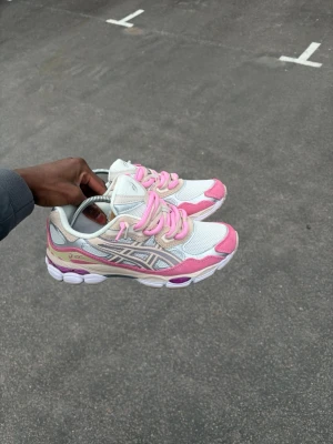 Double lacessed ASICS vita och rosa sneakers - Snygga sneakers från ASICS med vit mesh och rosa detaljer. Skorna har beige inslag och klassiska ASICS-loggan på sidan. Låga i modellen med rosa snören och en sportig design. Perfekta för dig som gillar färg och stil.