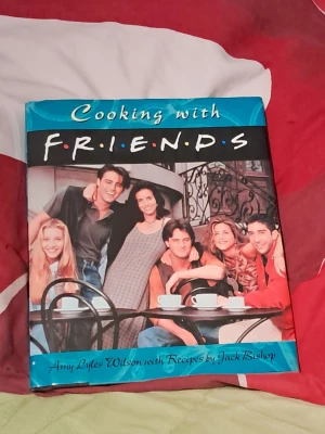 Friends kokbok - Säljer en kokbok med titeln 'Cooking with Friends', inspirerad av den ikoniska tv-serien Friends. Boken har ett färgglatt omslag med bilder från serien och innehåller recept av Jack Bishop. Perfekt för fans som vill laga mat med Friends-tema.--- Har dock en hälsning på insidan av boken