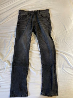 Grå slim fit jeans med tvättade detaljer - Snygga grå jeans i slim fit-modell med tvättade detaljer och klassisk femficksdesign. Jeansen har normal midja och raka ben, perfekta för en avslappnad och trendig stil. Materialet är mjukt och följsamt denim.