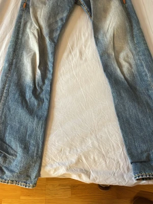 True Religion ljusblå jeans - Säljer ett par ljusblå jeans från True Religion med snygga slitningar och kontrastsömmar i gult. Jeansen har knäppning med knappar och klassisk femficksdesign. Casual passform Storlek W:33