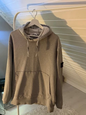Grå hoodie från Stone Island  - Säljer en Stone Island hoodie i grå färg.  Hoodien är i bra skick med normalt bruksslitage men inga större skador, hål eller fläckar. Den är väldigt bekväm och har den klassiska Stone Island-stilen med premium känsla och snygg passform.  Storlek är XXL, men den sitter mer som en vanlig L i passformen.  Personen på bilden är 190 cm lång, väger ca 80 kg och bär vanligtvis storlek L – vilket visar hur hoodien sitter i praktiken.  Pris: (du kan fylla i pris här) Storlek: XXL (passar som L)