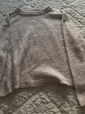 Beige stickad tröja med rund hals - Mysig beige stickad tröja med rund hals och långa ärmar. Tröjan har en enkel, rak passform och ribbade muddar vid ärmslut och nederkant. Perfekt för lager på lager och passar till det mesta i garderoben.