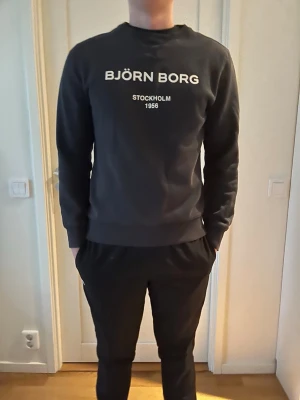Björn Borg sweatshirt - Snygg svart sweatshirt från Björn Borg med vit text på bröstet där det står 'BJÖRN BORG STOCKHOLM 1956'. Tröjan har rund halsringning, långa ärmar och ribbade muddar. Perfekt för en avslappnad och stilren look. Tröjan är lite använd men är fortfarande clean skriv om intresse finns.