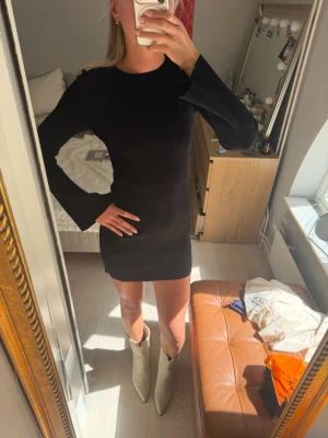 Svart ribbad kortklänning - Svart ribbad kortklänning med lång ärm och rund halsringning. Klänningen har en tight passform och är tillverkad i ett stretchigt materil. 