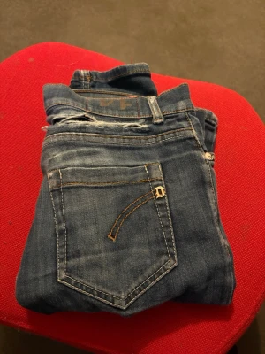 Blå slitna jeans med detaljer - Säljer ett par blå jeans med slitningar och hål på låret samt snygga detaljer på bakfickan. Jeansen har klassisk femficksdesign och är i ett mjukt denimtyg. Perfekta för en avslappnad och trendig look.