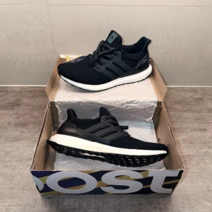 Adidas Ultraboost svarta sneakers - Svarta Adidas Ultraboost sneakers med stickad ovandel, vita Boost-sulor och svarta detaljer. Skorna har en sportig design med klassiska tre ränder på sidan och en bekväm, responsiv sula. Perfekta för dig som gillar streetwear och sportig stil.