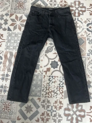 Svarta jeans från Jack & Jones 30/31 - Säljer ett par svarta raka jeans från Jack & Jones. Jeansen har klassisk femficksdesign, bälteshällor och knappgylf. Materialet är denim i bomull med en lätt tvättad look. Perfekta för en avslappnad och stilren outfit. Storlek 30/31 och använd en gång 