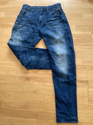 Replay - Snygga blå replay jeans i slim fit-modell med tydliga slitningar och tvättade detaljer på låren och knäna. Klassisk femficksdesign och knappgylf. Perfekta för en avslappnad och trendig look.