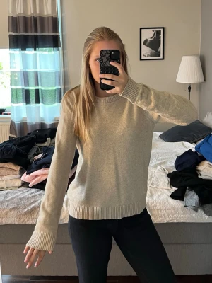Beige stickad tröja med rund hals - Mysig beige stickad tröja med rund halsringning och ribbade muddar vid ärmslut och nederkant. 