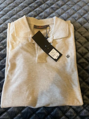 Beige pikétröja från Morris - Stilren beige pikétröja från Morris med klassisk krage och korta ärmar. Tröjan har en liten broderad logga på bröstet och är tillverkad i mjuk bomull. Perfekt för en avslappnad men snygg look.
