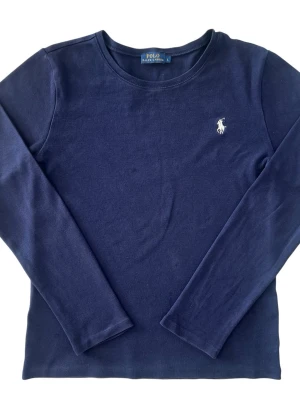 Äkta marinblå Polo Ralph Lauren sweatshirt (youth) - Mörkblå långärmad tröja från Polo Ralph Lauren i mjuk bomull. Tröjan har rund halsringning och en vit broderad logga på bröstet. Enkel och stilren design som funkar till många olika looks. Storleken är L i barnstorlek (XS/S  i vuxenstorlek)