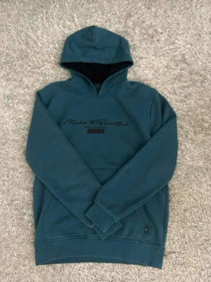 Hoodie med tryck - Snygg petrolblå hoodie med svart texttryck på bröstet där det står 'Make it Beautiful'. Hoodien har huva med svart insida och en klassisk, avslappnad passform. Perfekt för en chill och stilren look.