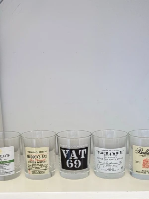 Whiskyglas med vintage etiketter - Fem whiskyglas i klarglas med tryckta etiketter från klassiska whiskymärken som Usher's, Hudson's Bay, VAT 69, Black & White och Ballantine's. Glasen är raka och cylinderformade, perfekta för samlare eller whiskyälskare som vill ha en unik touch på hyllan.