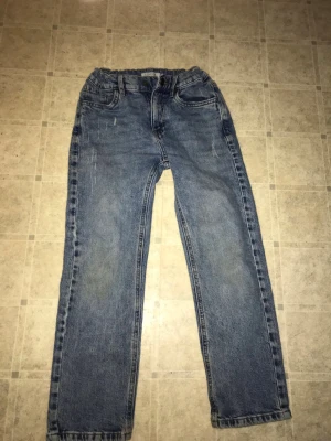 Blå raka jeans från Lindex - Säljer ett par klassiska blå jeans från Lindex i storlek 140. Jeansen har rak passform, resår i midjan och fyra fickor. Perfekta för en avslappnad stil och tillverkade i slitstarkt denimtyg.