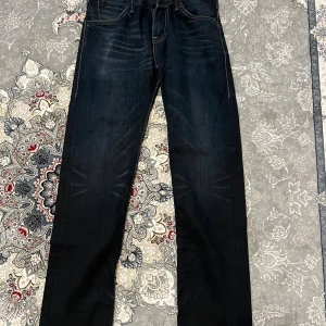 Mörkblå raka jeans från Levi's 29x32 - Snygga mörkblå jeans från Levi's med raka ben och klassiska kontrastsömmar. Jeansen har fem fickor och subtila slitningar framtill för en cool look. Perfekta för dig som gillar en tidlös och avslappnad stil. Storlek 29x32