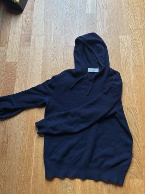 Sayless kashmirhoodie - Mysig mörkblå hoodie från Sayless i mjuk kashmir. Klassisk modell med huva och snörning, samt långa ärmar. Perfekt för dig som vill ha en stilren och bekväm hoodie i ett lyxigt material. Enda defekten är lite noppprig samt ett litet hål (bild 3) men inget man tänker på vid användning!