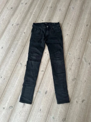 Gråsvarta jeans Replay modell Anbass. - Gråsvarta Replay Jeans i storlek 28x32. Modell Anbass, slim fit. Jeansen har smal passform hela vägen ner och stängs med dragkedja och knapp. Perfekta för en stilren och enkel look.