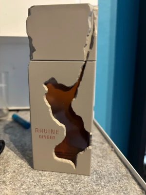 Ravine Ginger parfymflaska - Unik parfymflaska från Ravine i modellen Ginger. Flaskan är rektangulär med en ljusgrå yta och har ett coolt, oregelbundet utskuret fönster som visar den bärnstensfärgade vätskan inuti. Modern och stilren design som sticker ut i badrumshyllan.