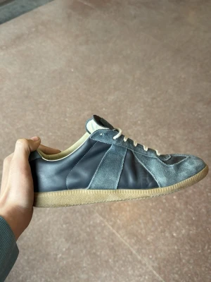 Gråblå sneakers i mocka och läder - Snygga sneakers i gråblå mocka och läder med vita snören och beige sula. Klassisk siluett med lågt skaft och retrovibbar. Perfekta för dig som gillar stilrena och tidlösa sneakers med en unik touch.