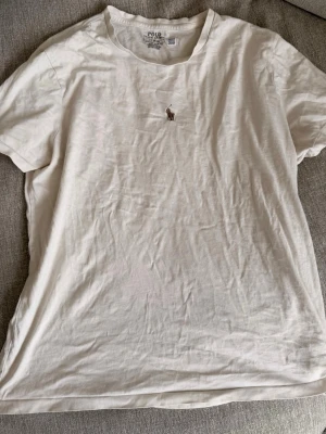 Vit t-shirt från Ralph Lauren - Vit t-shirt från Ralph Lauren med klassisk rund hals och broderad logga på bröstet. Modellen är custom slim fit och tillverkad i mjuk bomull, perfekt för en clean och stilren look.