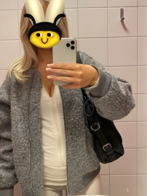 Grå teddy bomberjacka med ärmficka - Snygg grå bomberjacka i teddy-material med ribbade muddar och dragkedja framtill. Jackan har en extra ficka med dragkedja på ärmen och är fodrad på insidan. (Den är oversize i storleken så den passar xxs-s)
