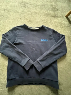 Mörkblå sweatshirt från BOSS - Snygg mörkblå sweatshirt från BOSS med rund halsringning och diskret blå logga på bröstet. Tröjan har långa ärmar och ribbade muddar vid ärmslut och nederkant. Perfekt för en clean och stilren look.