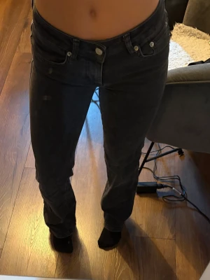 Svarta bootcut jeans med hög midja - Säljer ett par svarta bootcut jeans och låg midja. Jeansen har klassisk femficksdesign, silverfärgade knappar och detaljer. Snygg passform som sitter tajt upptill och släpper vid benen. Strl xs/short 