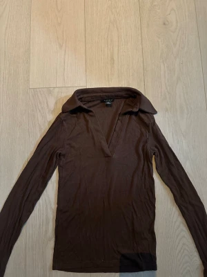Brun ribbad långärmad topp Amisu - Snygg brun långärmad topp från Amisu med djup v-ringning och bred krage. Toppen är ribbad och har en slim passform som sitter tajt mot kroppen. Perfekt att styla med jeans eller kjol för en trendig look.