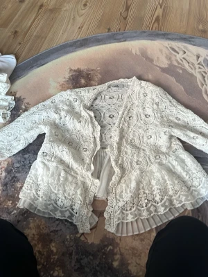 Vit spetsblus från Isolde - Superfin vit blus från Isolde i spets med vackra virkade detaljer och plisserad nederkant. Blusen har korta ärmar och en romantisk, luftig känsla. Perfekt för dig som gillar en feminin och bohemisk stil. Den är liten i storlek!!!