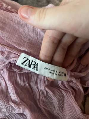 Ljusrosa pyjamaslinne från Zara - Ljusrosa populär blus från Zara med tunna axelband och volangdetaljer. Tillverkat i ett skirt, mjukt material som känns luftigt och bekvämt. Perfekt för dig som vill ha en söt och romantisk look.