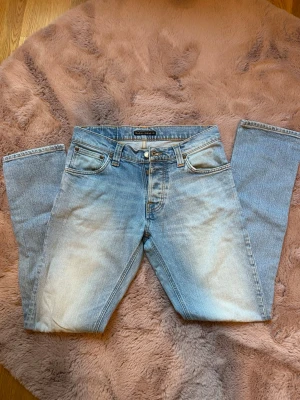 Nudie 30x32 Grim Tim - Snygga ljusblå jeans från Nudie med klassisk femficksdesign och raka ben. Jeansen har en lätt tvättad look och är tillverkade i bomull med en liten mängd stretch för extra komfort. Perfekta för en avslappnad och trendig stil.