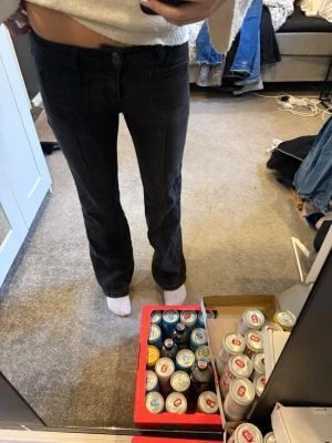 bootcut raka jeans med fickor - Säljer ett par svarta jeans med raka ben och stora framfickor och fickor med knappar där bak. Jeansen har synliga sömmar och klassisk knappgylf. Perfekta för dig som gillar en stilren och enkel look. Finns mått på bilderna.