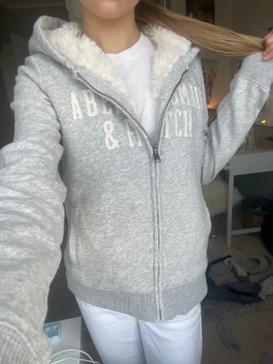 Grå hoodie från Abercrombie & Fitch - Säljer en sååå snygg hoodie från Abercrombie & Fitch i storlek S😍 den har en dragkedja och fluffig päls innanför luvan, magen och ryggen. Äääälskar men tyvärr lite för stor för mig. Har inte använts mycket och är i ett mycket gott skick. Hör av er för frågor eller fler bilder!