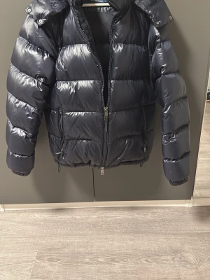 Mörkblå pufferjacka från Polo Ralph Lauren - Snygg mörkblå pufferjacka från Polo Ralph Lauren med glansig finish och broderad logga på bröstet. Jackan har hög krage, dragkedja framtill, två sidofickor med dragkedja och justerbar nederkant. Perfekt för kalla vinterdagar. Jackan är sällsynt och går inte att få tag på längre. Passa på nu nör priserna är lägre, hör av er vid minsta fundering✅
